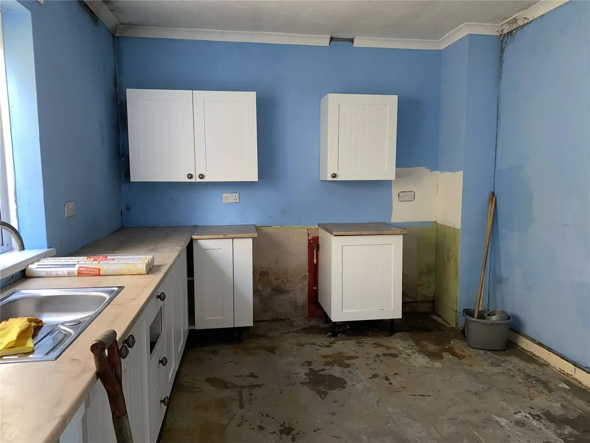 Kitchen before refurbishment — gutted units, bare walls, unfinished floor